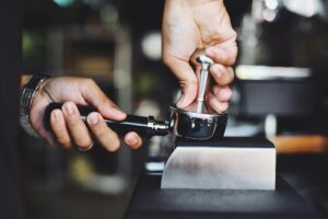 Close-up of a barista tamping coffee grounds using an espresso tamper.